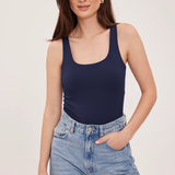 A woman modeling a navy blue scoop-neck tank top paired with light-wash blue jeans against a plain light background.