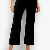 A model wearing black cropped wide-leg trousers with a subtle sheen, paired with a white top and white heeled sandals, set against a plain white studio background.