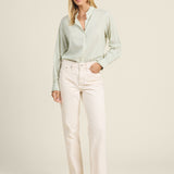 Woman wearing a light green blouse and white pants on a beige background