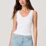 Woman wearing a white tank top and light blue jeans against a plain background