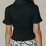 Person wearing a black textured blouse with short sleeves and a patterned white skirt.