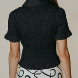 Person wearing a black textured blouse with short sleeves and a patterned white skirt.