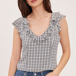 A woman wearing a black and white gingham check sleeveless top with ruffle trim, paired with blue jeans, against a plain light background.