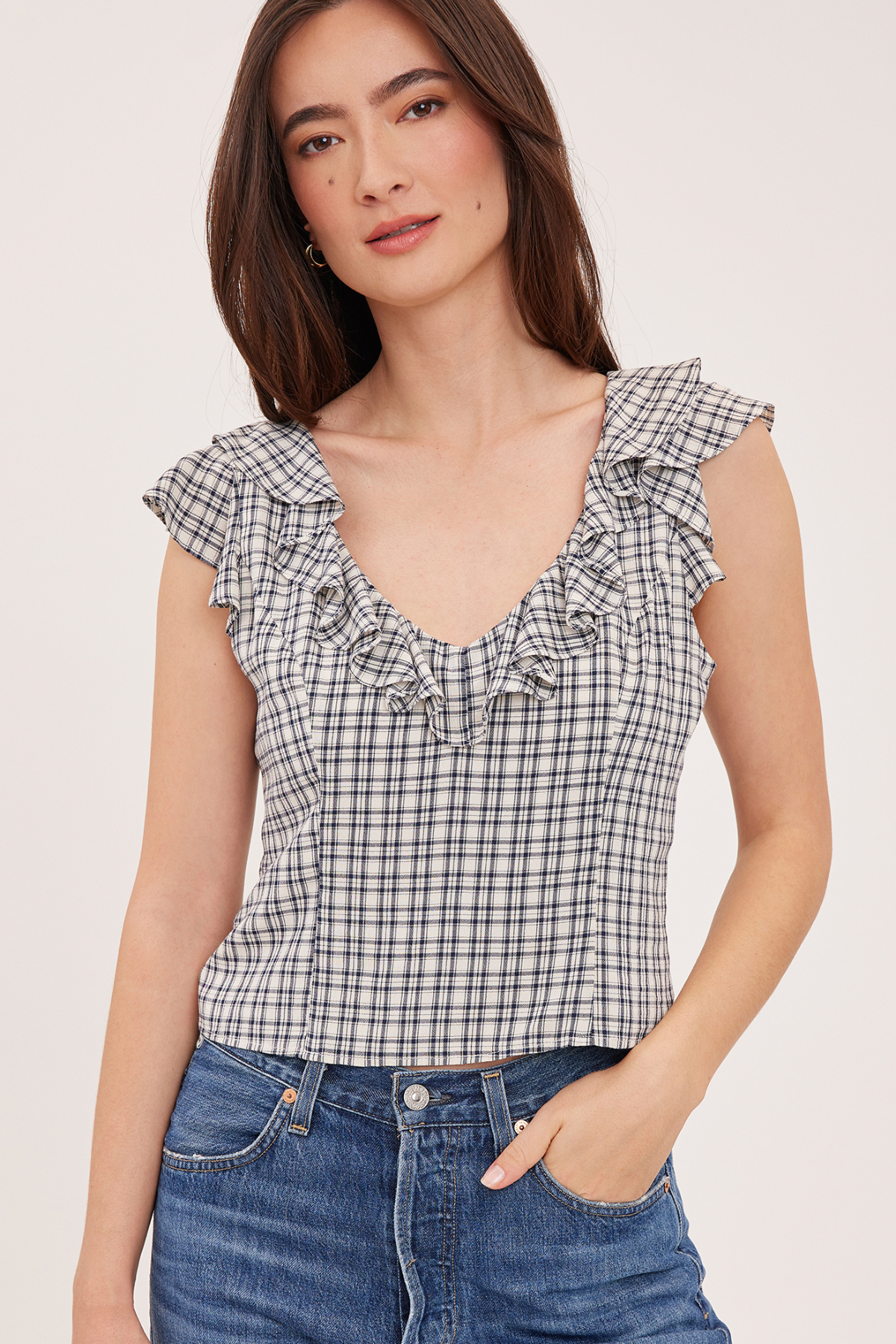 A woman wearing a black and white gingham check sleeveless top with ruffle trim, paired with blue jeans, against a plain light background.