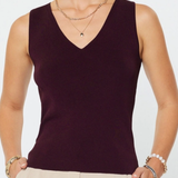 Woman wearing a dark purple sleeveless top and beige pants against a white background