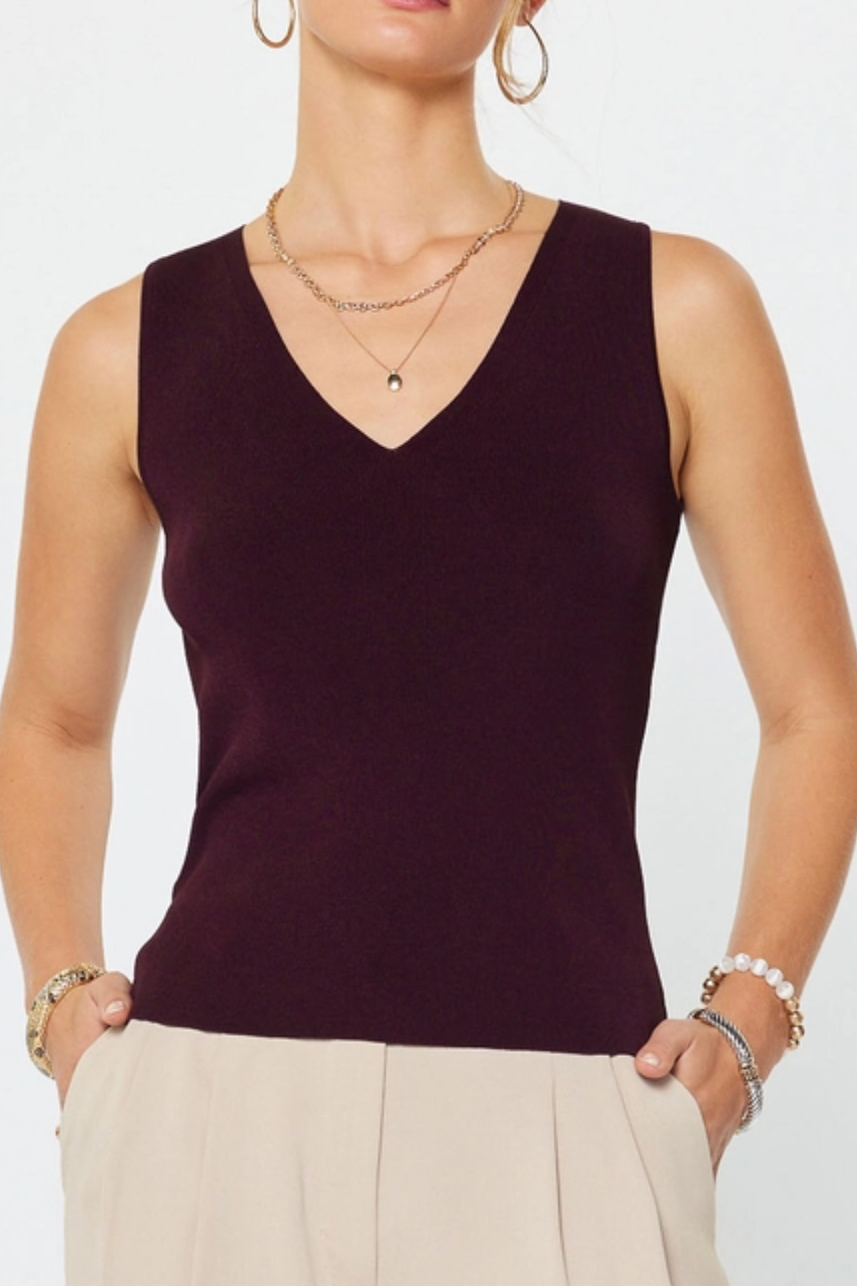 Woman wearing a dark purple sleeveless top and beige pants against a white background