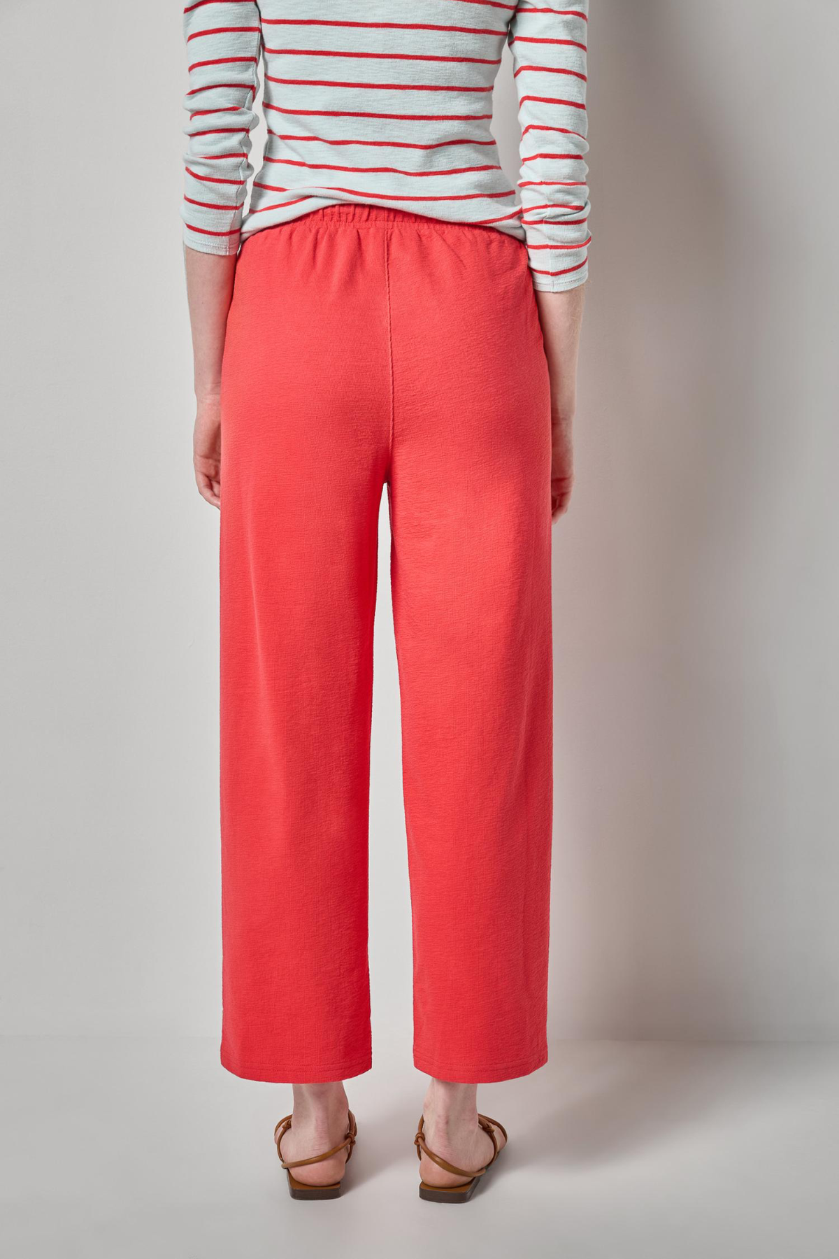 Person wearing a striped shirt and coral pants on a plain background