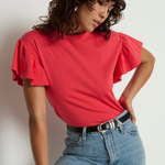 Woman wearing a red blouse with ruffled sleeves and blue jeans against a plain background