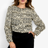 A woman modeling a long-sleeve cropped knit top with a black and beige abstract textured pattern, paired with black trousers, against a plain white studio background.