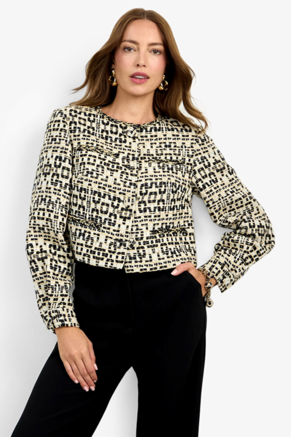 A woman modeling a long-sleeve cropped knit top with a black and beige abstract textured pattern, paired with black trousers, against a plain white studio background.