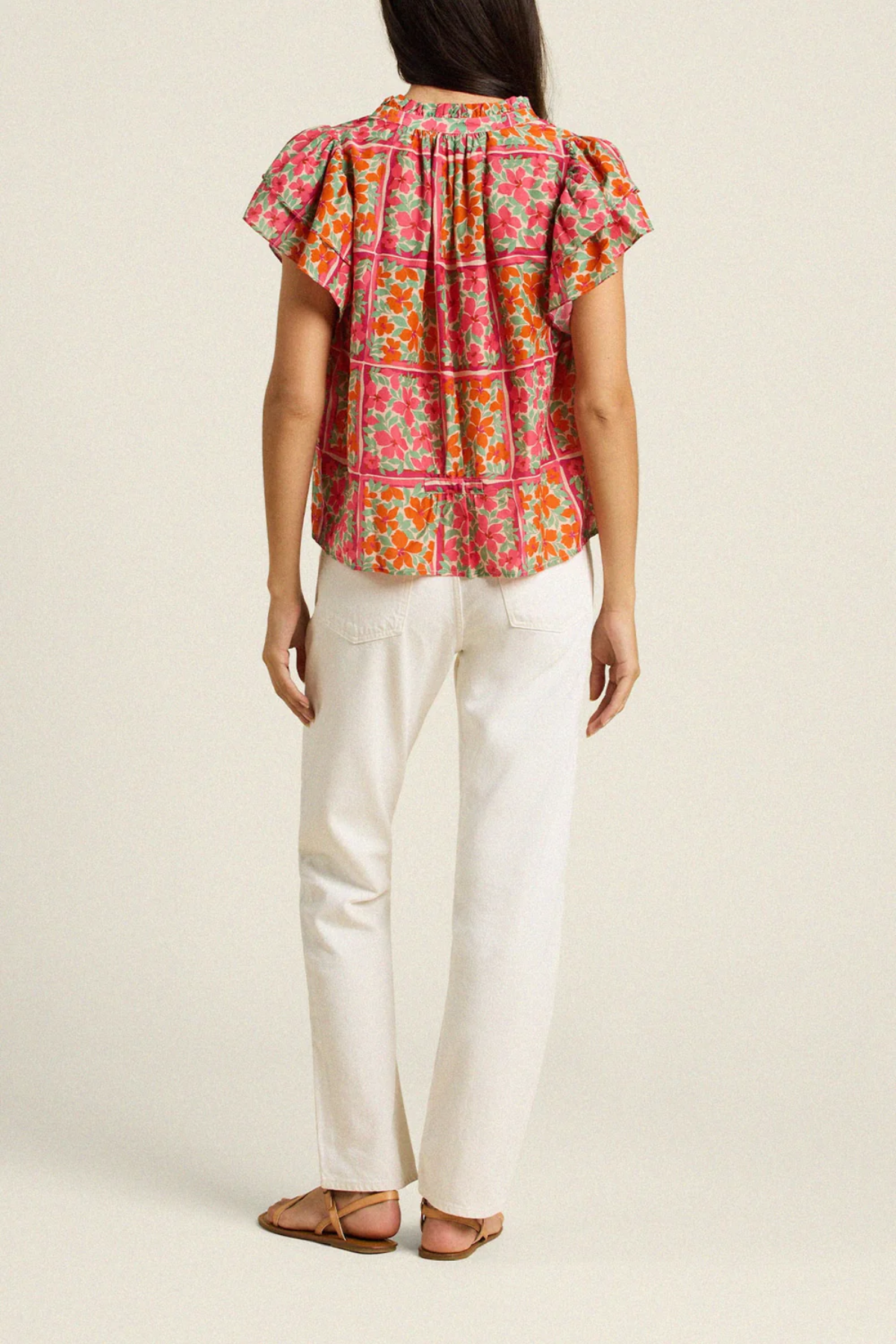 back of woman in floral blouse and white denim on white background 
