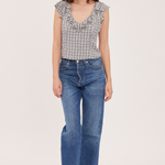 A woman modeling a sleeveless black and white gingham top with ruffle trim and blue wide-leg jeans against a plain light background.