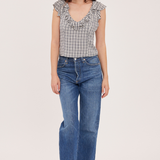 A woman modeling a sleeveless black and white gingham top with ruffle trim and blue wide-leg jeans against a plain light background.