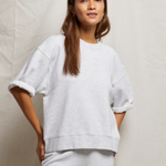 Woman wearing a light gray sweatshirt and pants against a neutral background