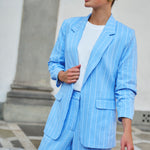 Woman wearing a light blue pinstripe suit with a white top outdoors.