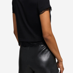 A woman shown from the back wearing a black short-sleeve top with lace trim at the hem and sleeves, paired with black faux-leather shorts with lace trim, against a light gray studio background.