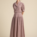 Woman wearing a pink checkered dress with puff sleeves against a beige background