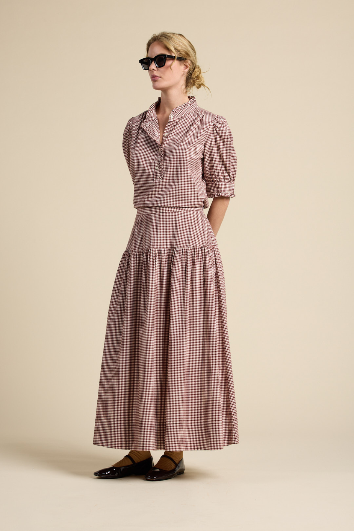 Woman wearing a pink checkered dress with puff sleeves against a beige background