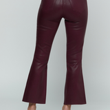 A person shown from the back wearing high-waisted, flared trousers in a deep burgundy faux-leather material, paired with a matching long-sleeve top and pointed-toe heels, against a light gray studio background.