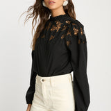 Woman wearing a black lace blouse and white pants on a light gray background