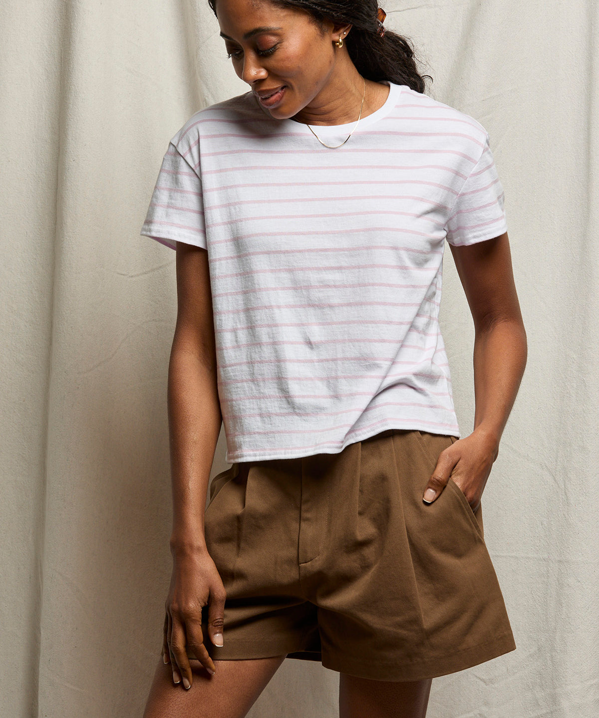 Woman wearing a striped shirt and brown shorts against a neutral background