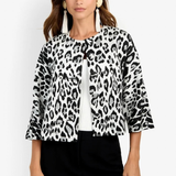A woman modeling a black and white leopard print jacket with three-quarter sleeves, worn over a white ribbed top and black pants, against a plain white background.