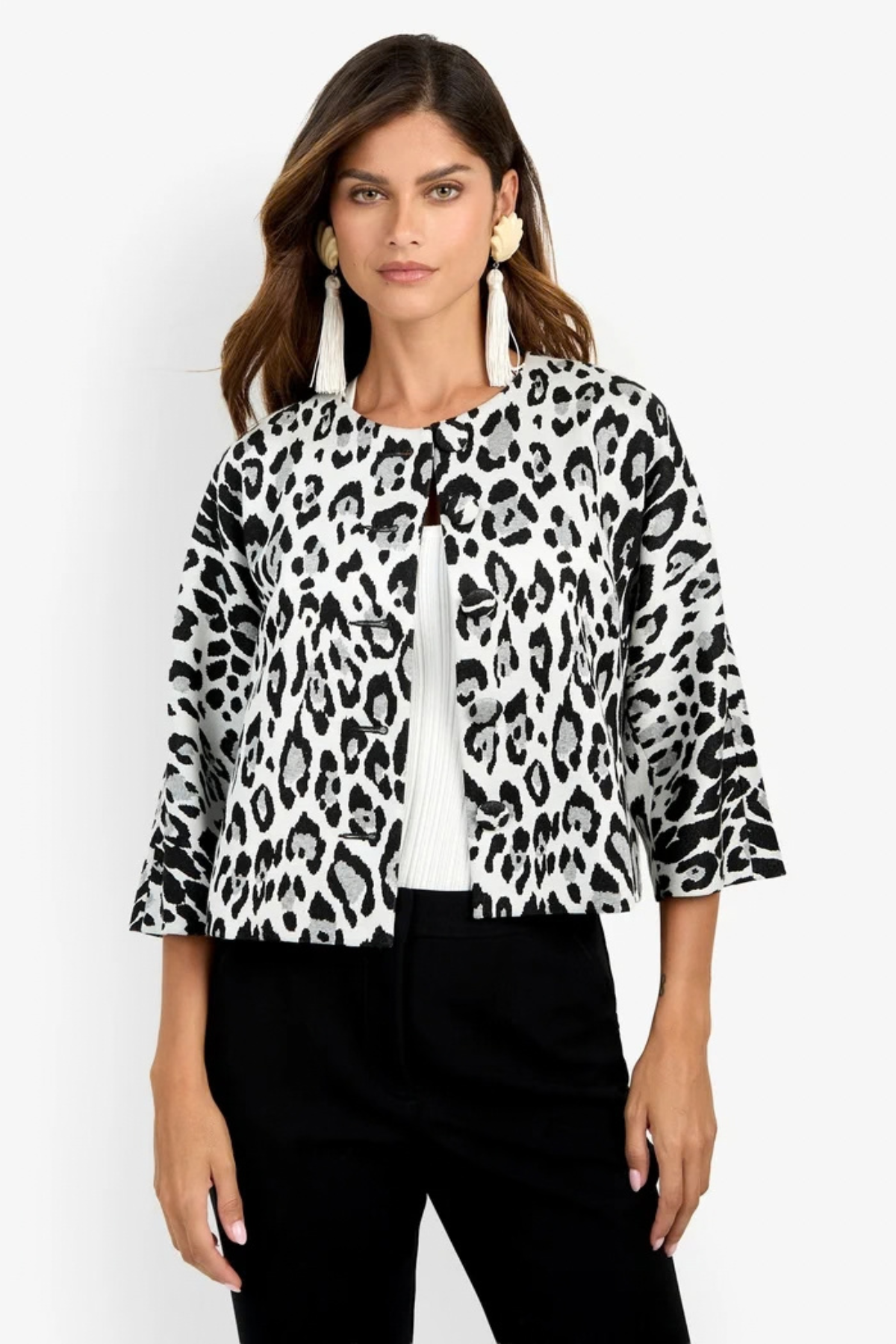 A woman modeling a black and white leopard print jacket with three-quarter sleeves, worn over a white ribbed top and black pants, against a plain white background.