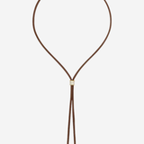 A brown leather cord necklace with a small gold-toned square charm and dangling cord ends, shown on a plain light gray background.