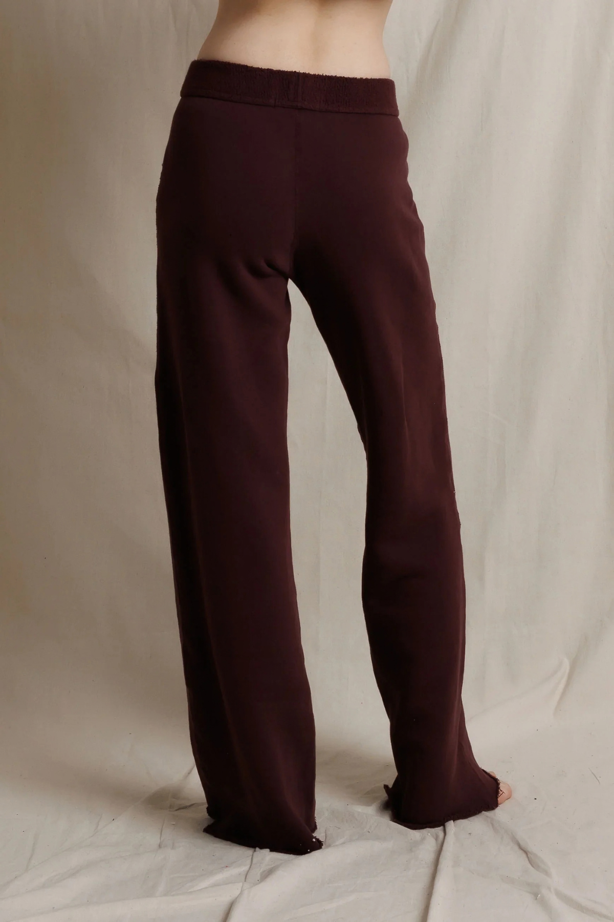 A person wearing loose, straight-leg knit pants in a deep burgundy or maroon shade, shown from the waist down against a draped off-white fabric backdrop.