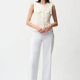 Woman wearing a sleeveless beige top and white pants on a white background