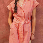 woman in striped dress standing by brick wall outside 