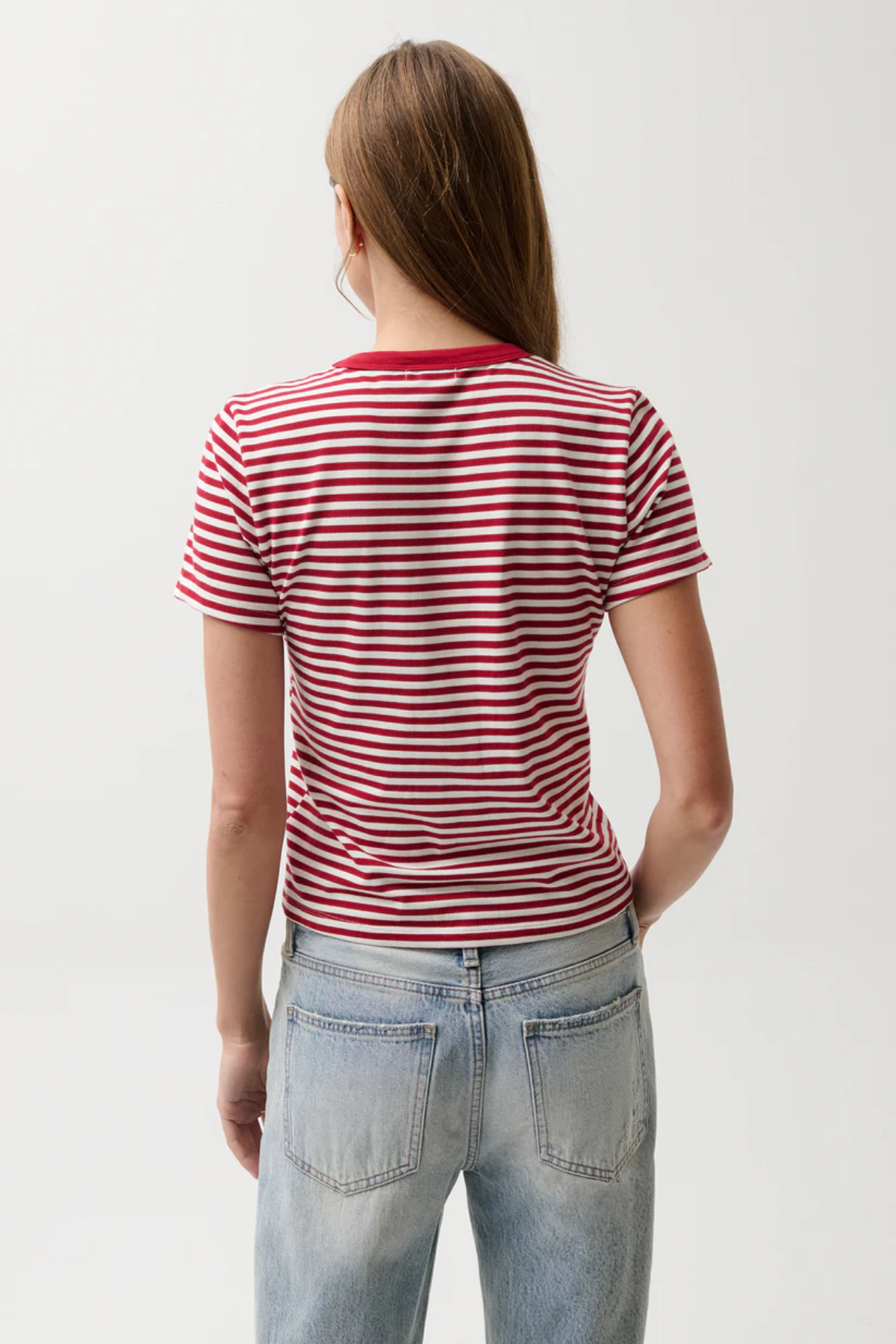 Person wearing a red and white striped shirt and light blue jeans on a plain background