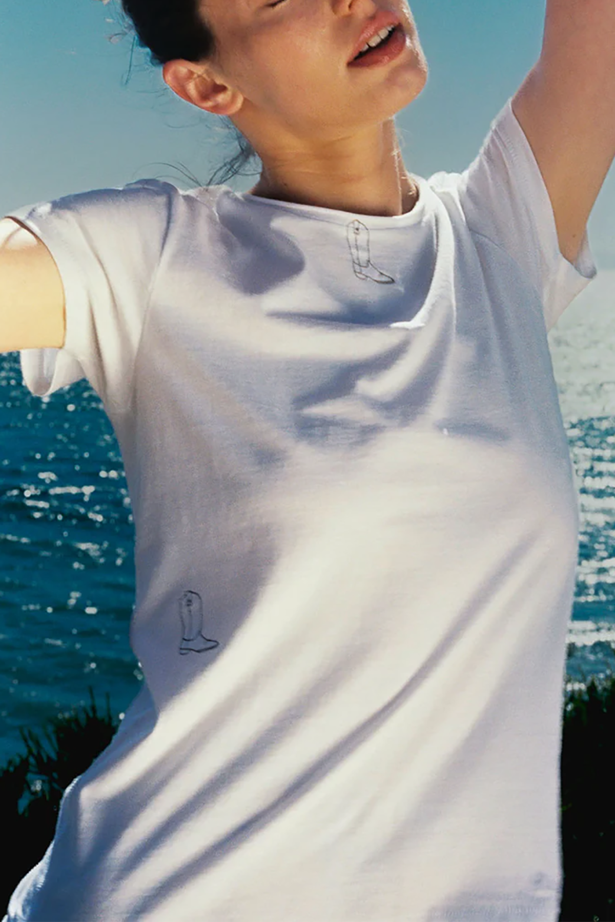Person wearing a white t-shirt with a logo, standing by a body of water.