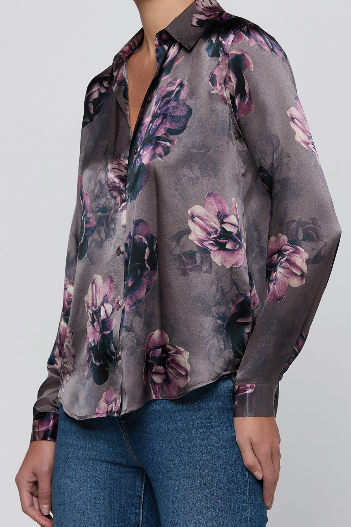 A woman wearing a long-sleeve satin blouse with a dark gray base and a purple, pink, and black floral print, paired with blue jeans.