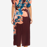 A woman modeling a midi dress from the back, featuring a deep burgundy base with a large peach and blue floral print on the upper back and shoulder area.