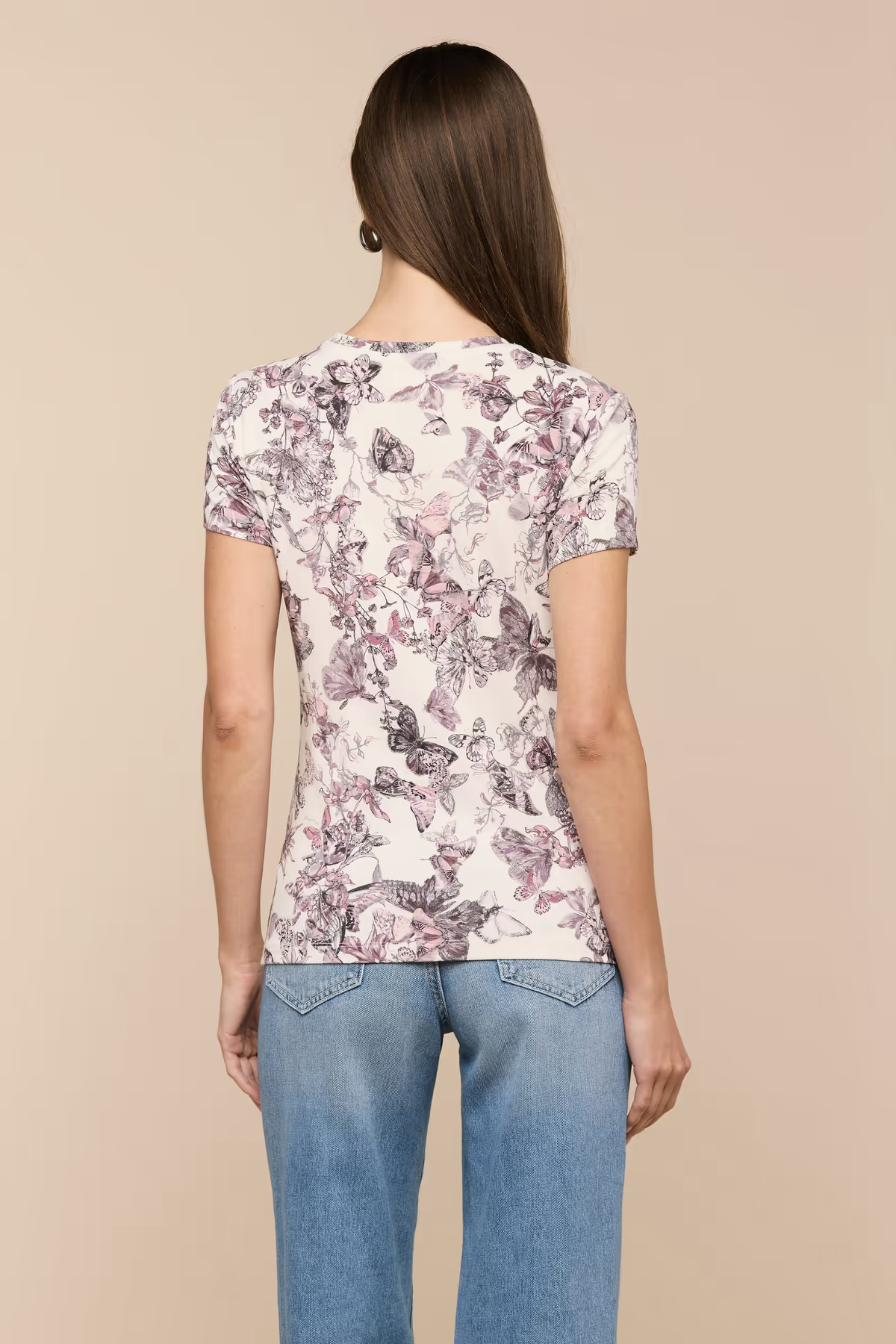 Woman wearing a floral t-shirt and blue jeans on a beige background