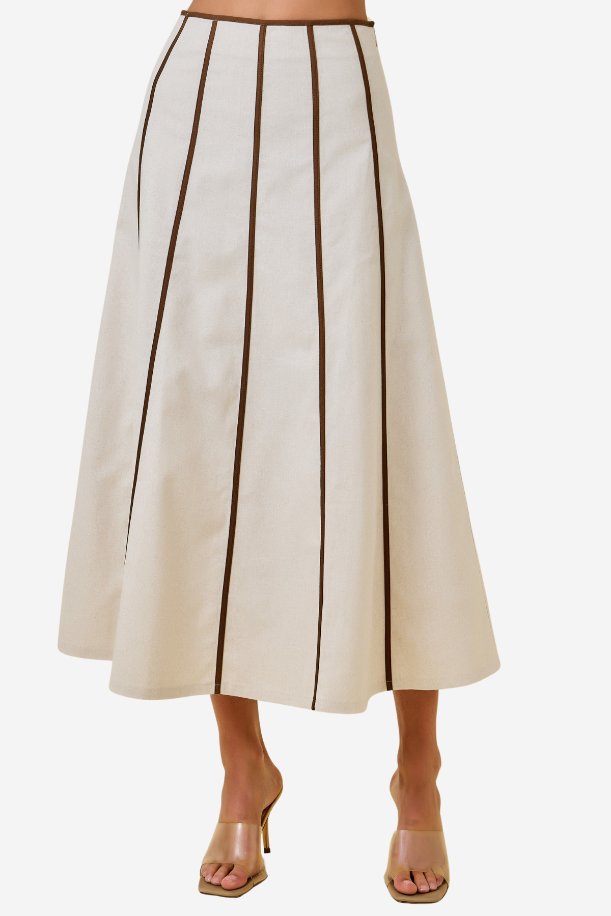 An off-white A-line midi skirt with vertical dark brown pleats, shown on a model wearing clear high-heeled sandals against a light gray background.
