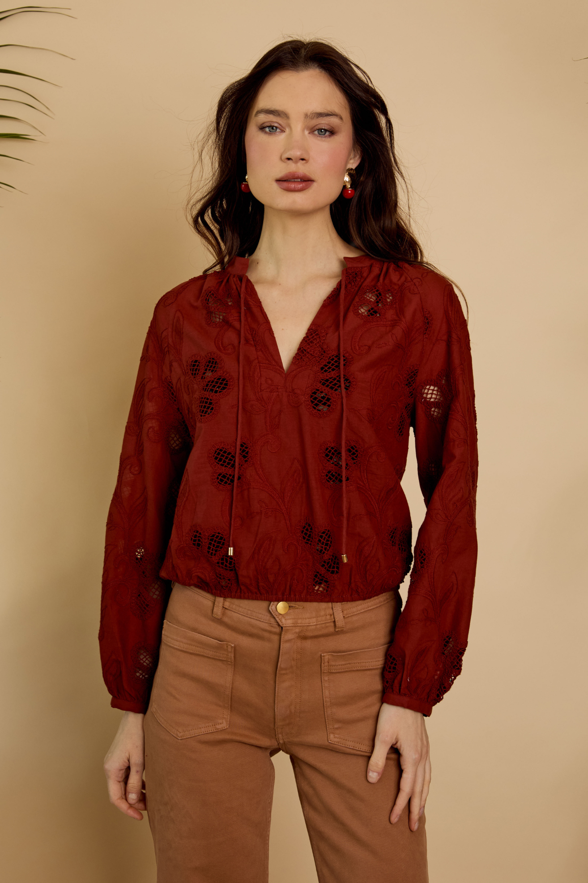 Woman wearing a red blouse with black floral patterns and brown pants against a beige background