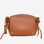 A tan leather crossbody bag with a curved top, tassel details on the straps, and small gold-tone hardware, shown against a plain light gray background.