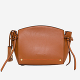 A tan leather crossbody bag with a curved top, tassel details on the straps, and small gold-tone hardware, shown against a plain light gray background.