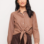 A woman modeling a brown and beige vertically striped button-down shirt tied at the waist, paired with dark brown pants, against a plain light gray background.