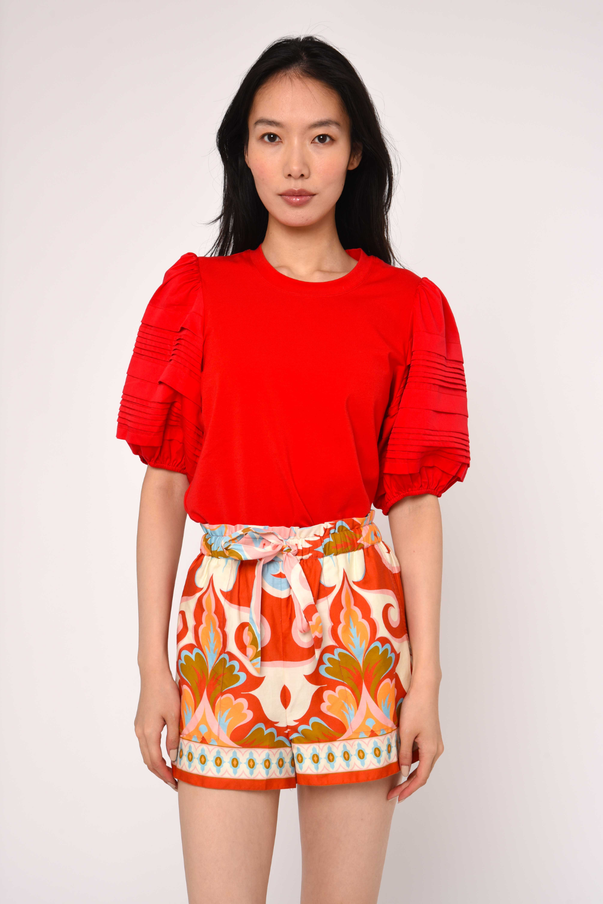 Woman wearing a red top and patterned shorts against a white background