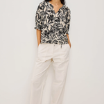 Woman wearing a black and white patterned blouse with white pants on a white background