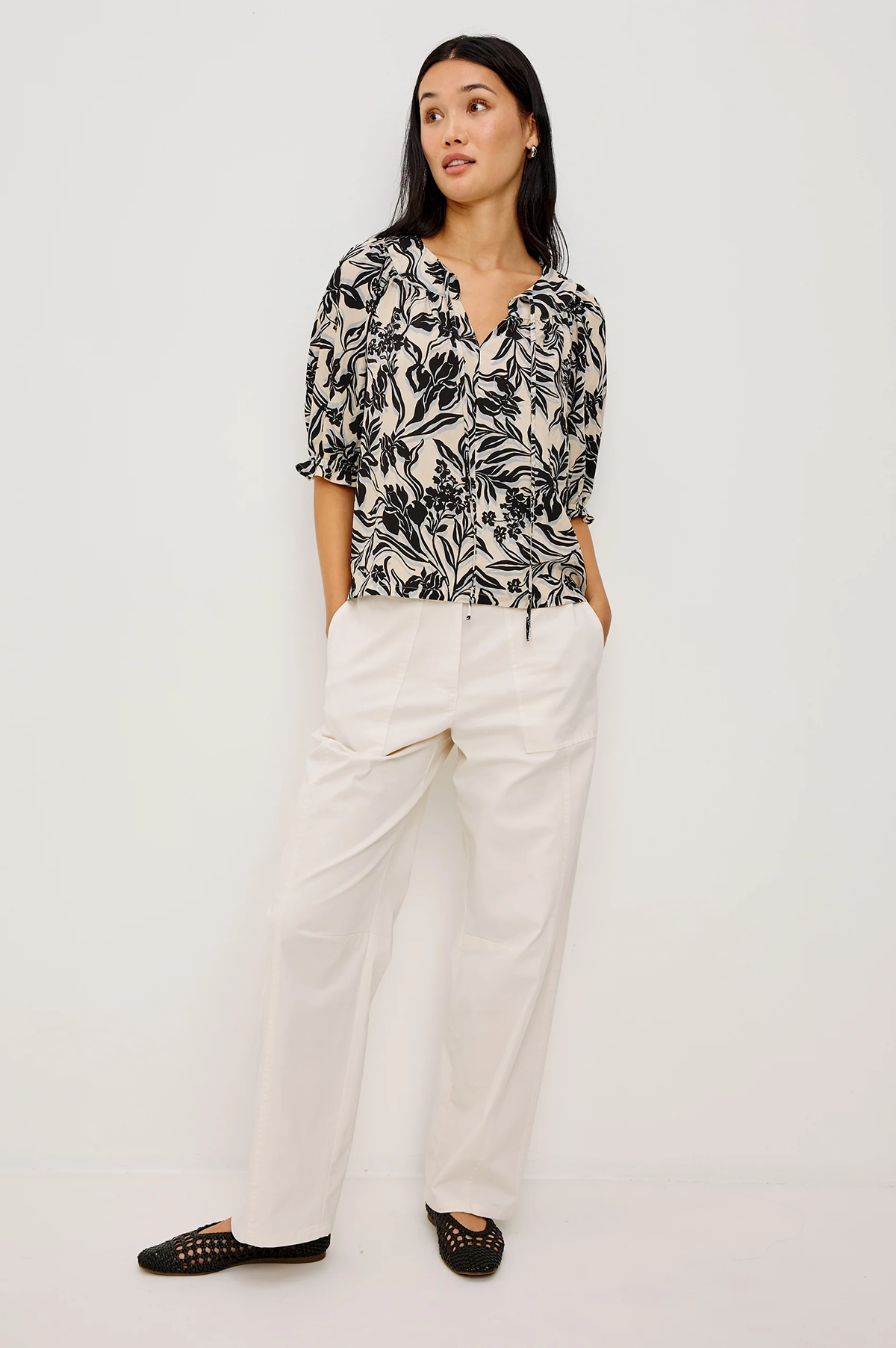 Woman wearing a black and white patterned blouse with white pants on a white background