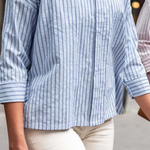 Close-up of a person wearing a blue and white striped shirt with rolled-up sleeves.