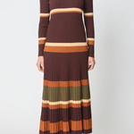 A woman modeling a long-sleeve ribbed knit mock-neck midi dress with horizontal stripes in dark brown, rust orange, olive green, and cream, paired with brown suede ankle boots against a light gray studio background.