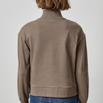 Person wearing a brown jacket and blue jeans on a plain background