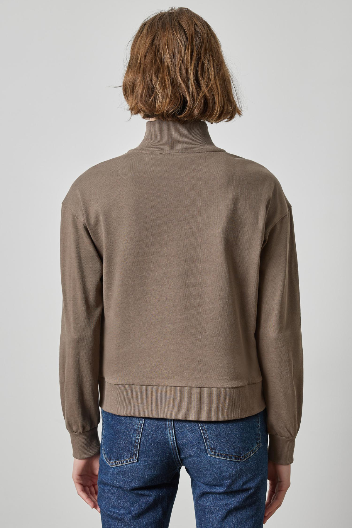 Person wearing a brown jacket and blue jeans on a plain background