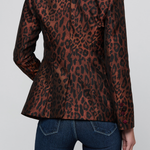 A woman shown from the back wearing a brown and black leopard-print blazer with dark red piping on the collar and cuffs, paired with dark blue jeans, against a light gray studio background.