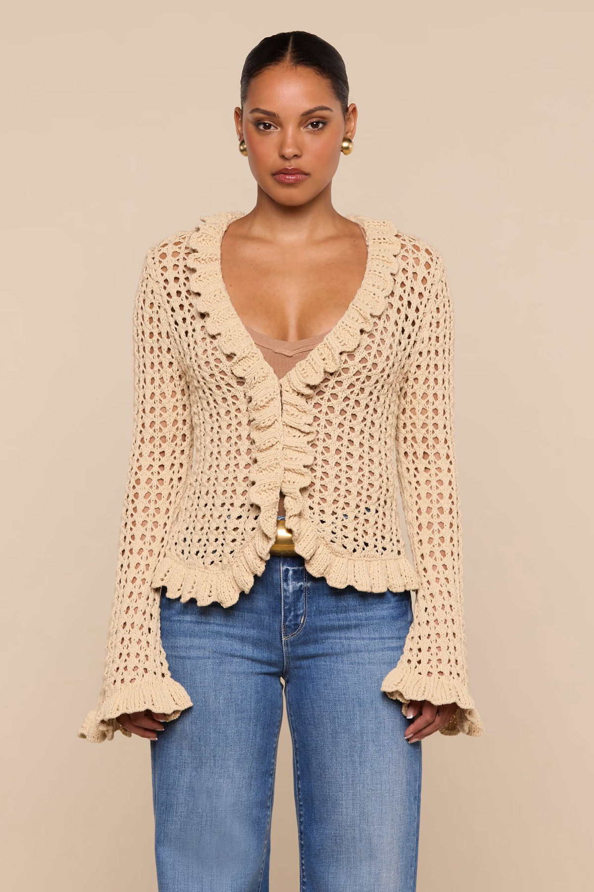 Woman wearing a beige crochet cardigan and blue jeans on a beige background